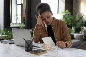 Young woman writing in a notebook while working on a laptop in a stylish indoor setting.